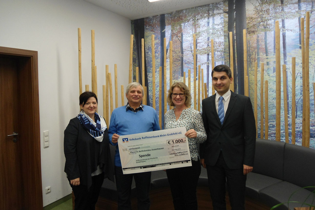 Zwei Frauen und zwei Männer stehen vor einem Fenster. Ein Mann und eine Frau halten einen Spendenscheck in der Hand 