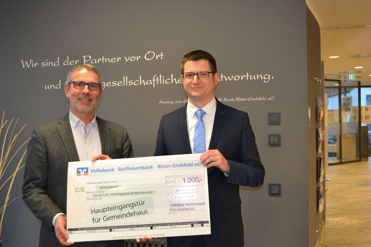 Zwei Männer stehen vor einer Wand und halten einen Spendenscheck in der Hand 