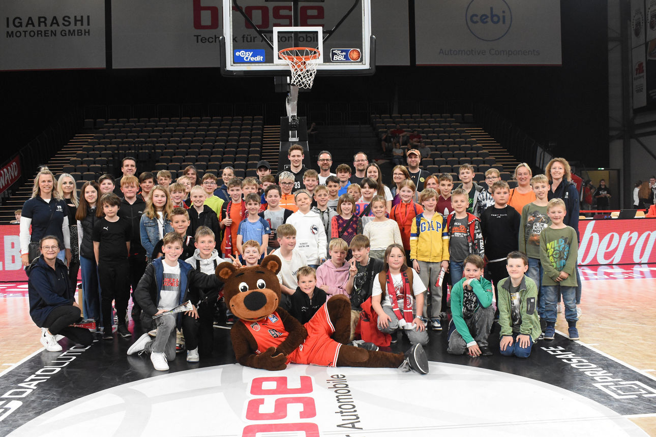 Eine große Gruppe von Kindern und Erwachsenen posiert gemeinsam auf einem Basketballfeld