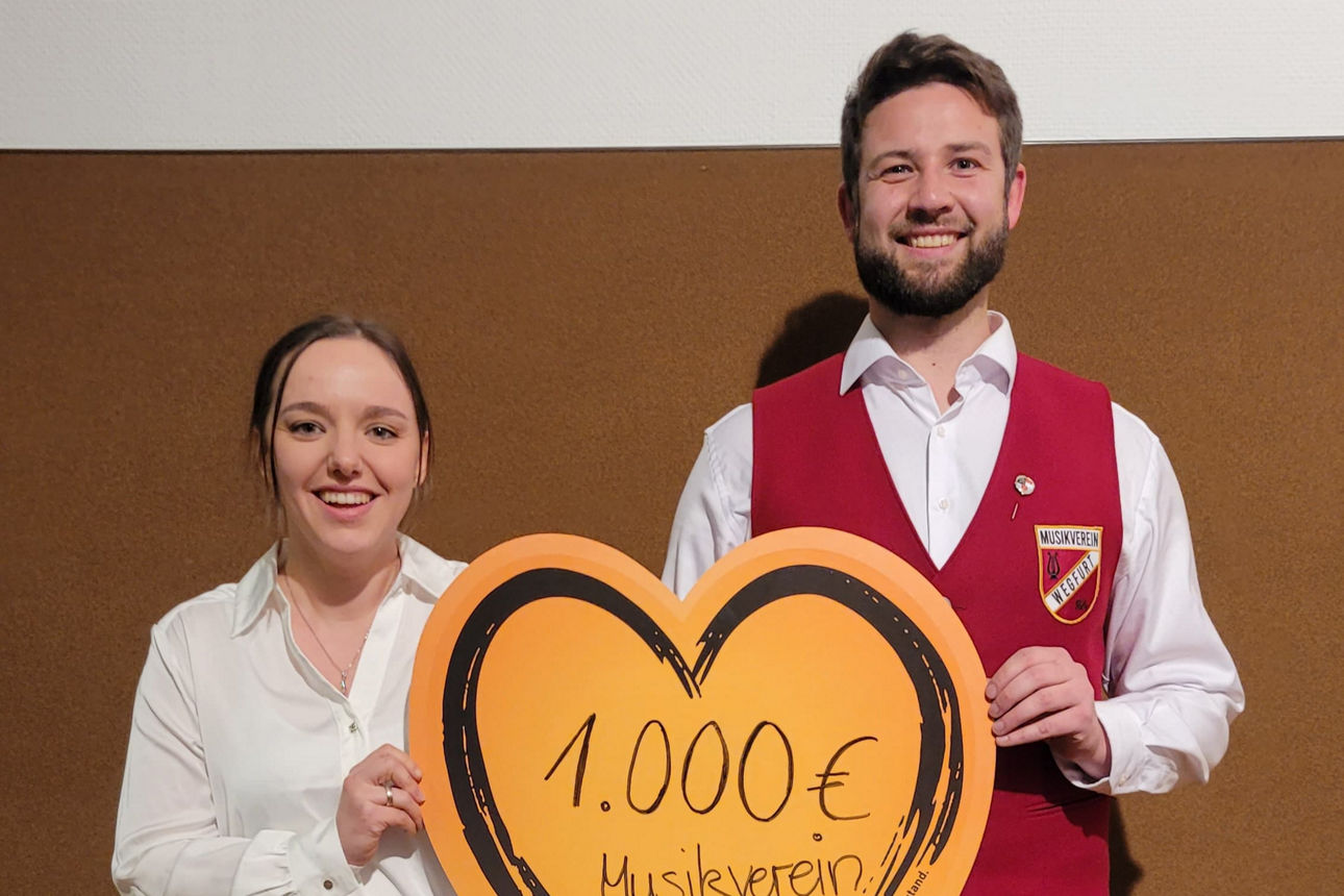 Zwei Personen, eine Frau und ein Mann in Tracht, halten gemeinsam ein großes, orangefarbenes Herz 