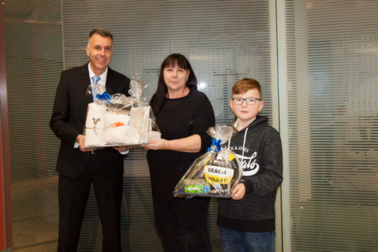 Ein Mann in Anzug gibt einer Frau ein Geschenk, während ein Junge rechts danaben auch ein Geschenk in der Hand hält