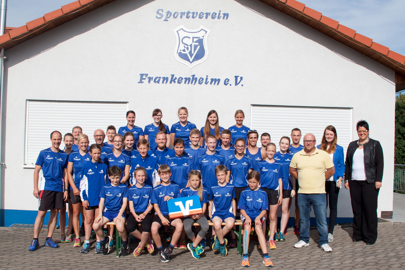 Mitglieder eines Laufvereins mit blauen Trikots vor Vereinsheim.Bankberaterin auf der rechten Seite und VR-Bank Logo mittig