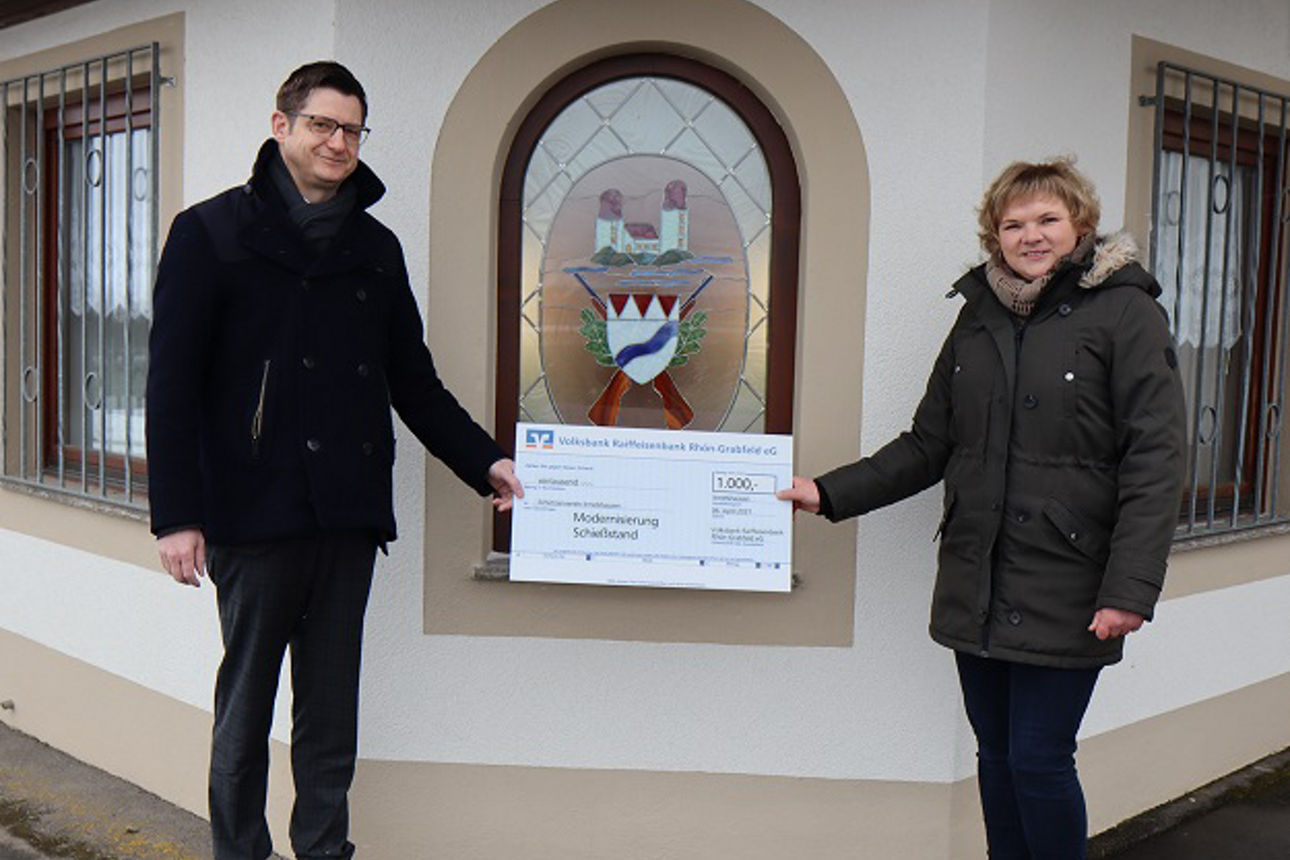 Vor einem Haus stehen ein Mann und eine Frau, die einen Spendenscheck in der Hand halten