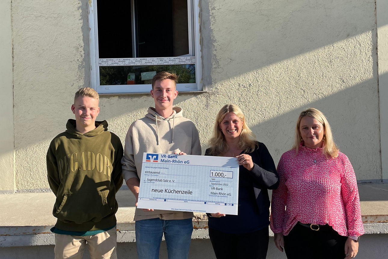 Zwei Männer und zwei Frauen stehen vor einem Haus ein Mann und eine Frau halten einen Spendenscheck in der Hand 