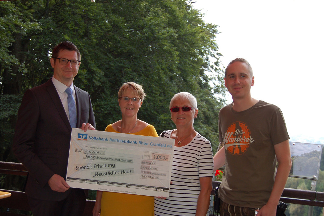 Zwei Frauen und zwei Männer stehen vor einem Geländer, während zwei von ihnen einen Spendenscheck halten 