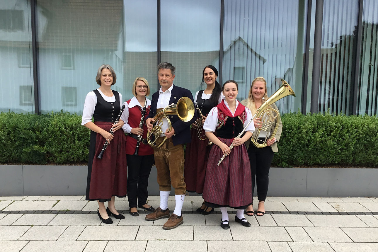 Sechs Musikanten stehen vor einem Gebäude wobei einige von ihnen Instrumente in der Hand halten