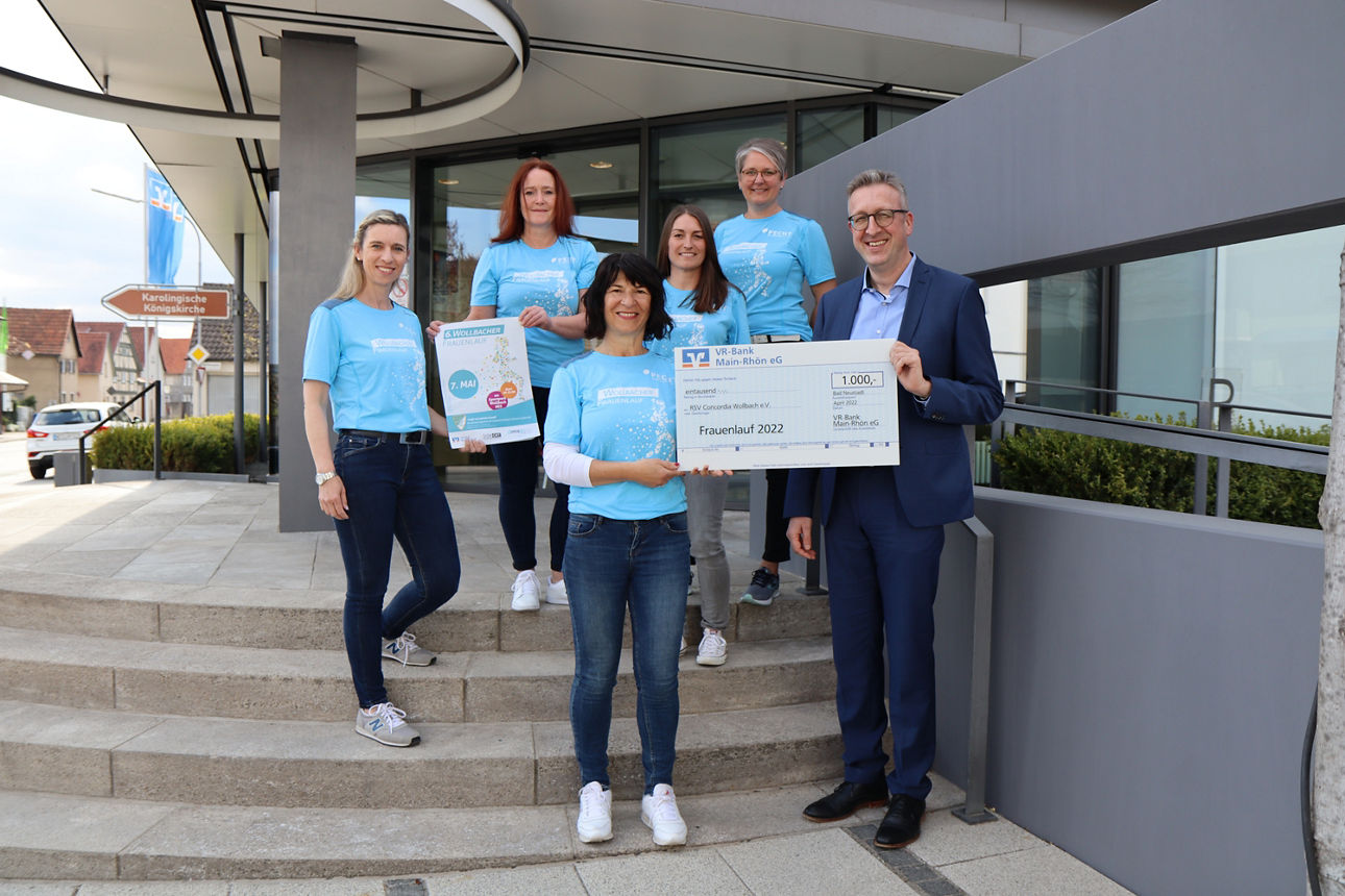 Sechs Personen stehen vor einem Gebäude ein Mann und eine Frau halten einen Spendenscheck in Höhe von 1.000 Euro in der Hand