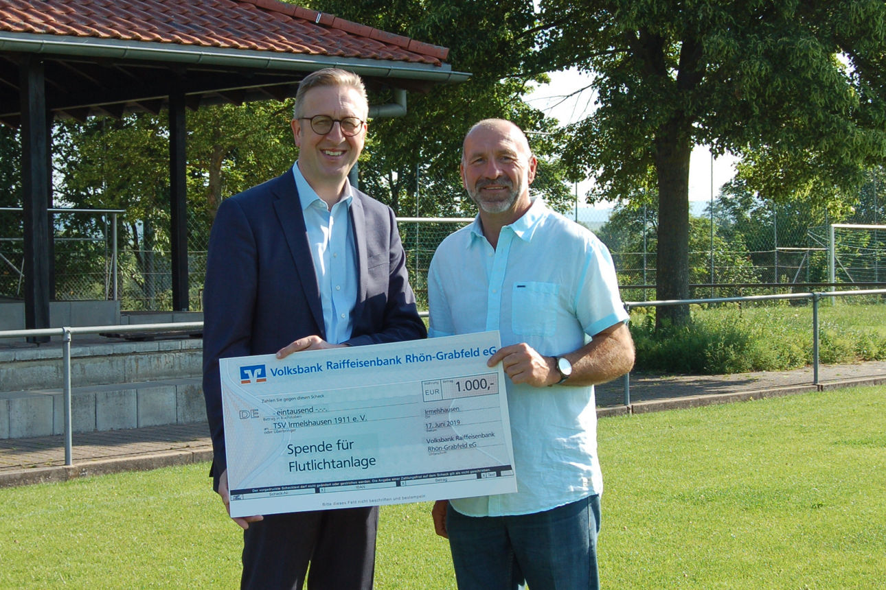 Zwei Männer stehen auf einem Rasen und halten einen Spendenscheck in der Hand 