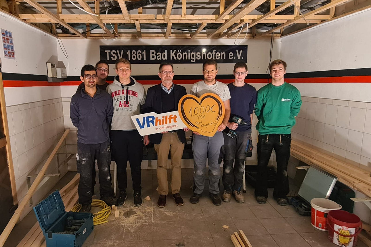 Eine Gruppe von sieben Personen steht in einem Raum mit Bauarbeiten; zwei Personen halten ein großes Herz