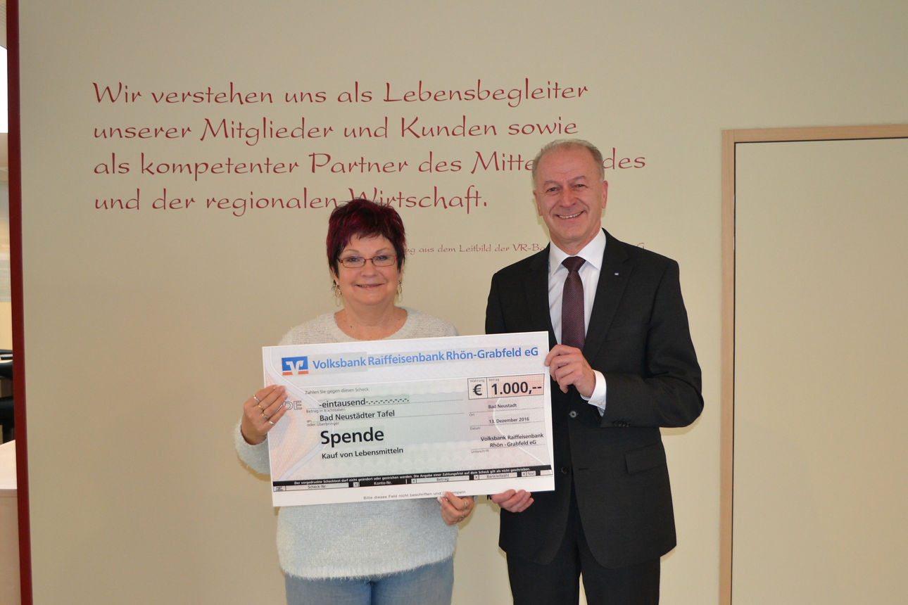 Frau und Mann stehen vor einer Wand und halten einen Spendenscheck in der Hand 