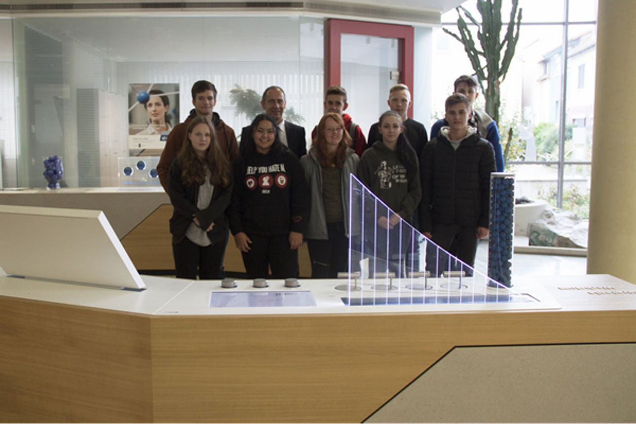 Zehn Schüler stehen vor einem Pult in einem Gebäude und blicken in die Kamera 