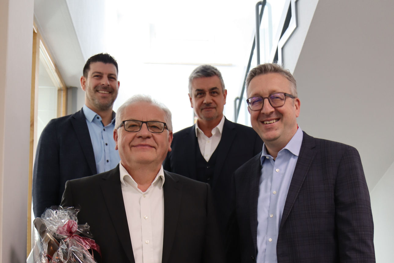 Auf einer Treppe stehen vier Männer, die Anzüge tragen in zwei Reihen 