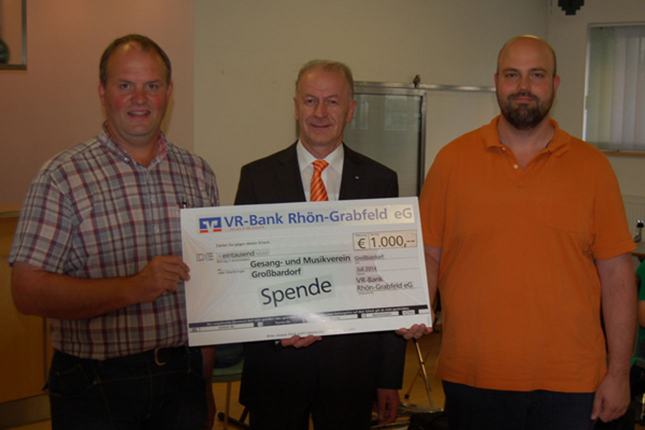 Drei Männer stehen vor einer Wand und halten einen Spendenscheck in der Hand 