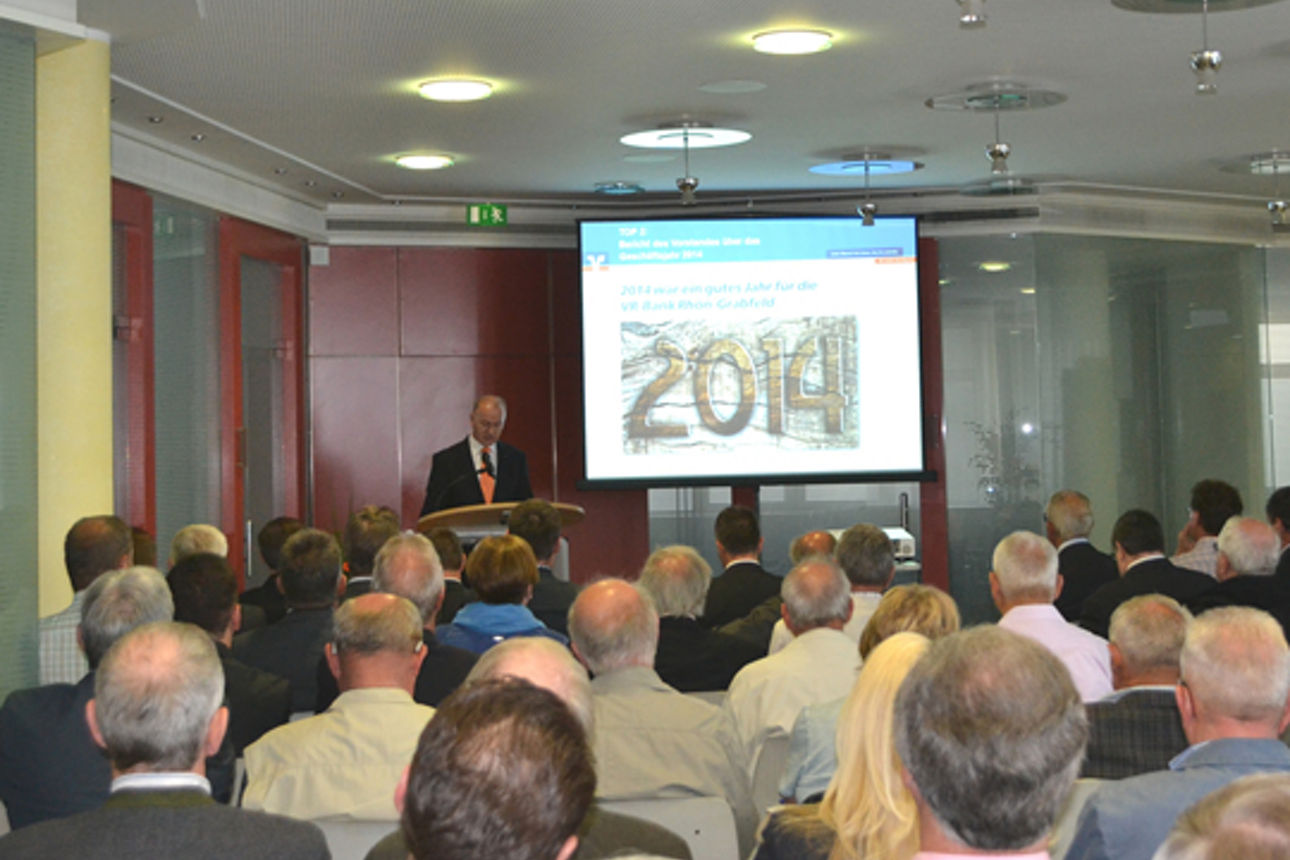 In einem Raum sitzen viele Menschen und schauen auf einen Mann der eine Präsentation hält 