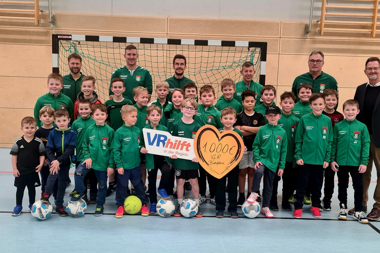 Eine große Gruppe von Kindern und Erwachsenen steht in einer Sporthalle vor einem Fußballtor zwei Personen halten ein Schild