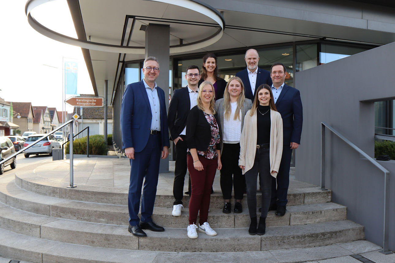 Auf einer Treppe vor einem Bankgebäude stehen vier Frauen und vier Männer 