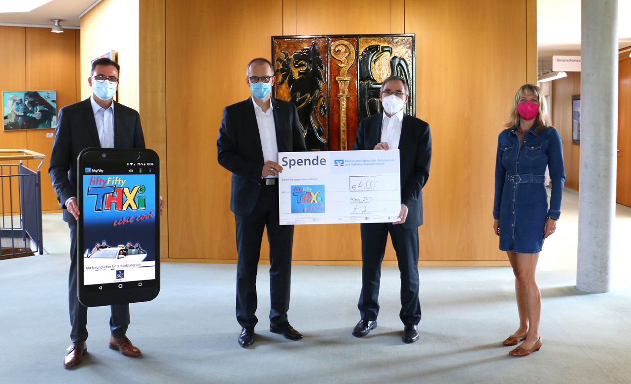 Drei Personen mit Gesichtsmasken halten einen Scheck