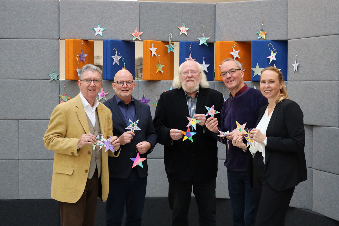 Vertreterinnen und Vertreter der Volksbank und der Telefonseelsorge laden zum Basteln von Weihnachtssternen für den guten Zweck ein.