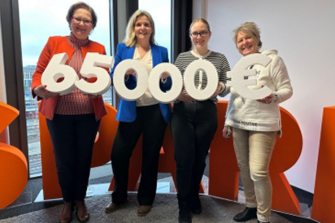 Gruppenbild von vier Frauen, die die symbolische Spendensumme aus Styroporzahlen hochhalten