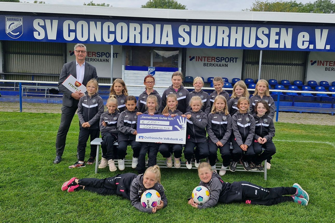 Junge Fußballerinnen erhalten einen Spendenscheck für neue Trainingsanzüge