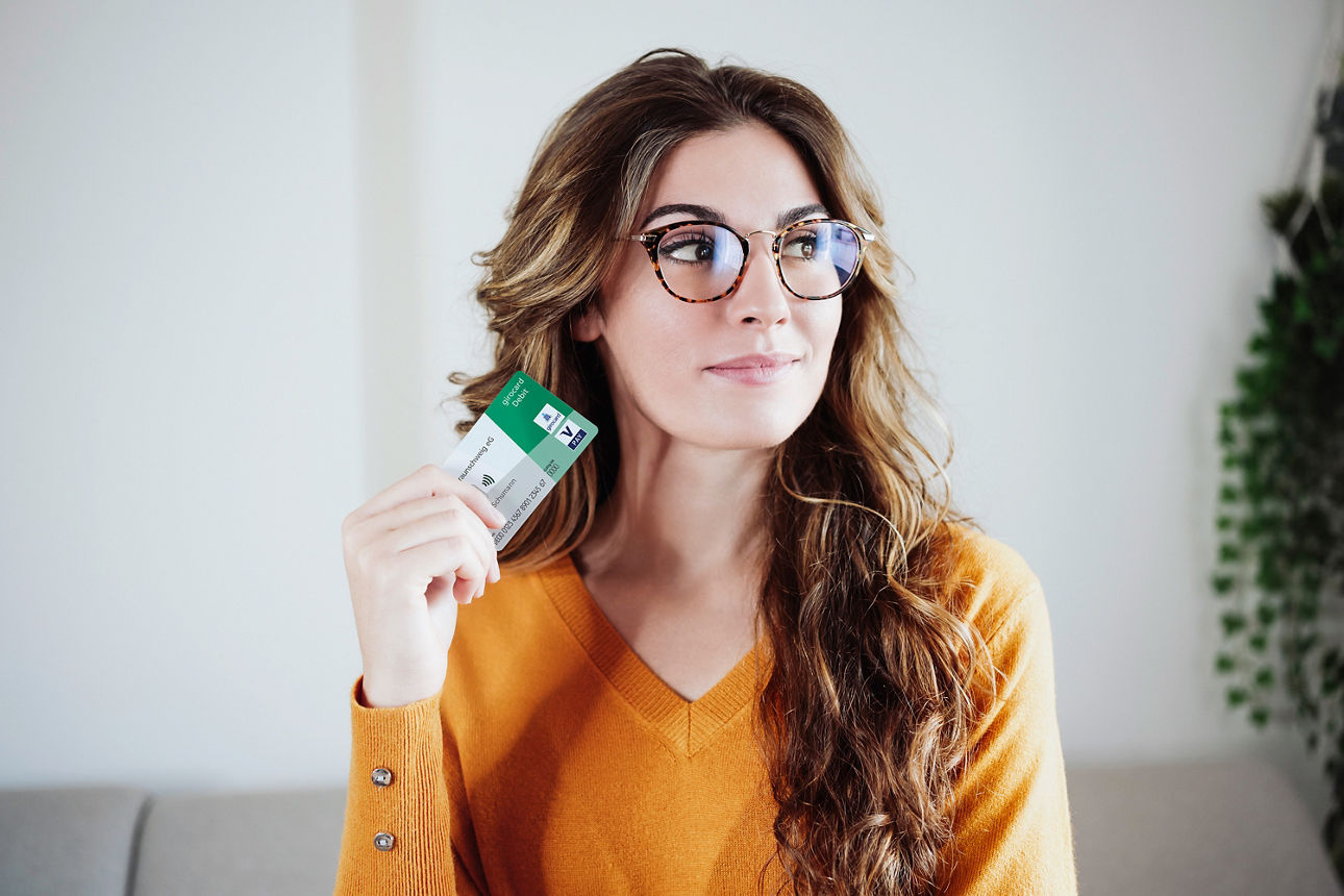 Junge Frau mit Brille hält eine girocard in die Kamera und schaut leicht grinsend zur Seite