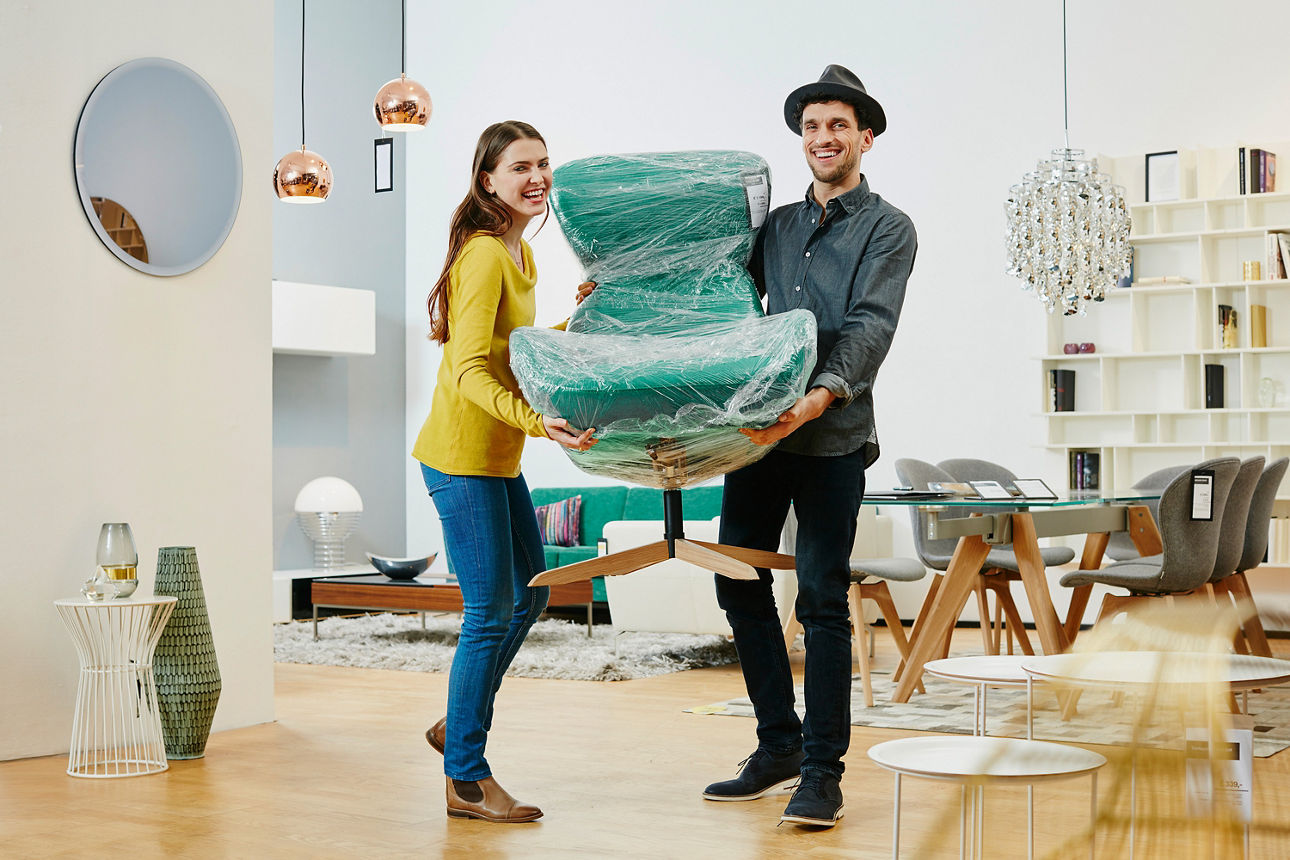 Eine Frau und ein Mann mit Hut tragen ein Möbelstück