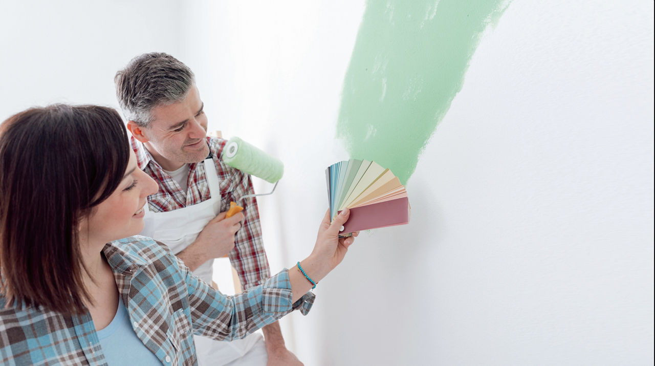 Ein Mann und eine Frau streichen eine Wand grün und vergleichen die Farben