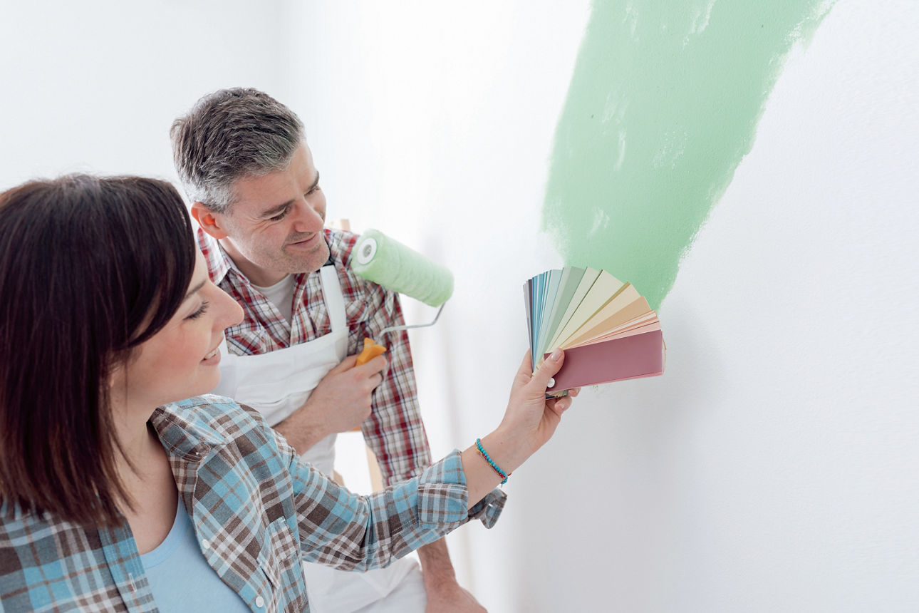 Ein Mann und eine Frau streichen eine Wand grün und vergleichen die Farben