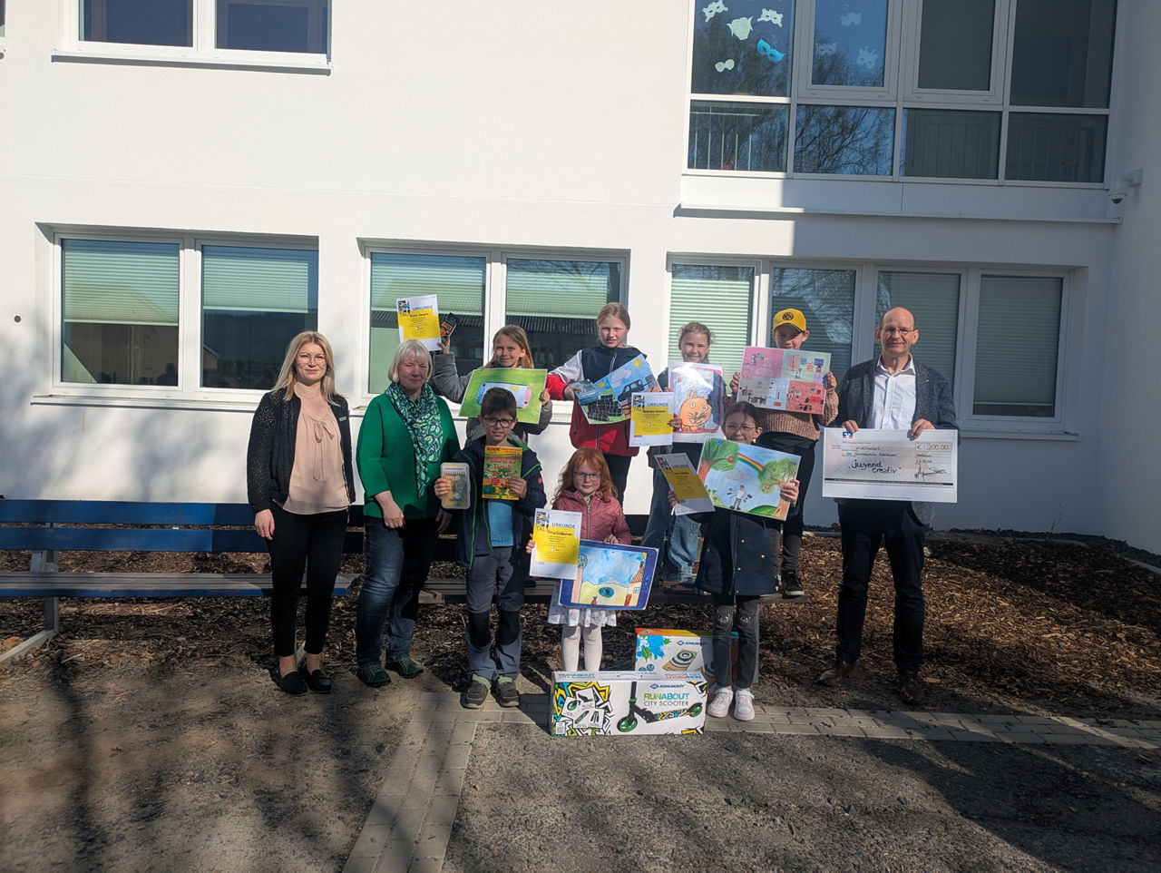 Die Gewinner des Jugend creativ Wettbewerbs stehen mit ihren Zeichnungen und den Gewinnen vor einem großen Gebäude.