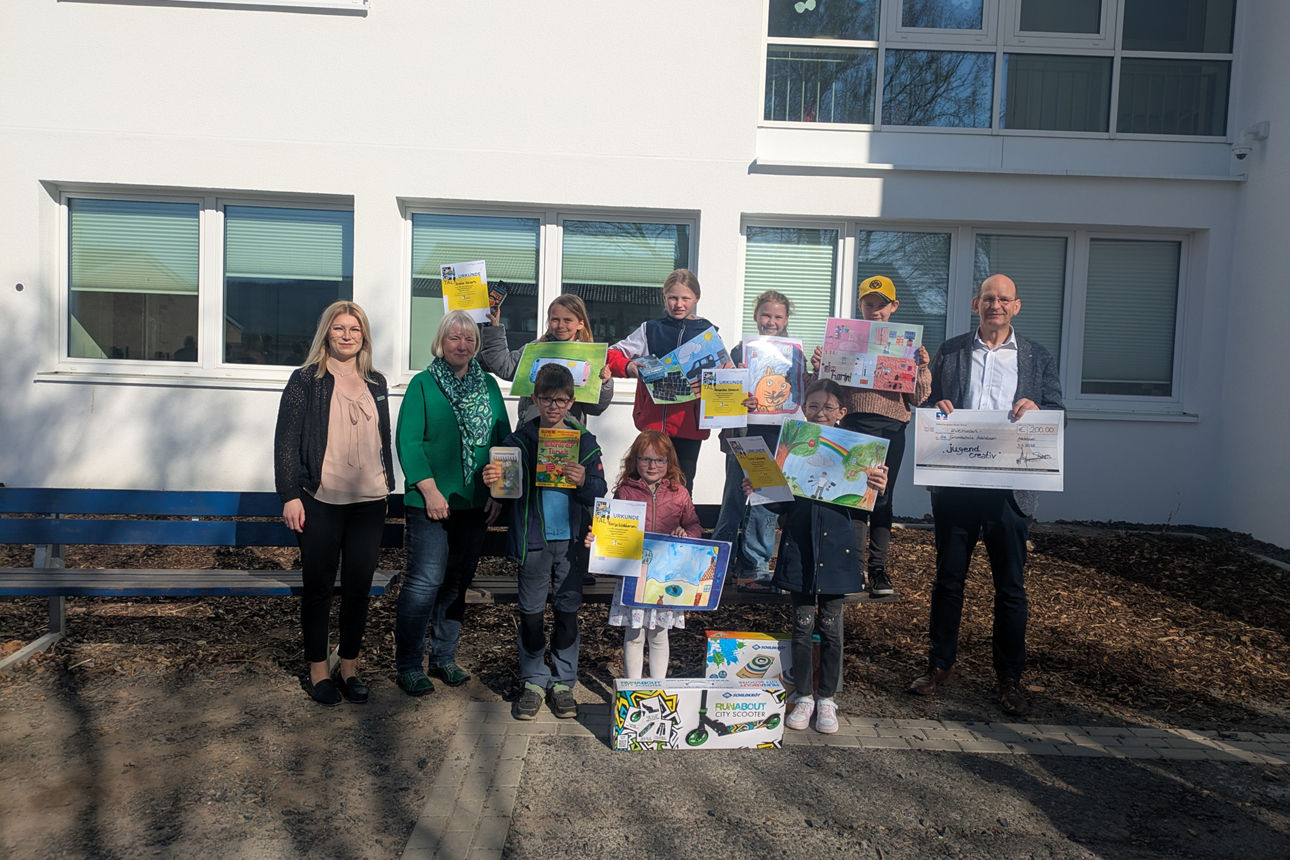 Die Gewinner des Jugend creativ Wettbewerbs stehen mit ihren Zeichnungen und den Gewinnen vor einem großen Gebäude.