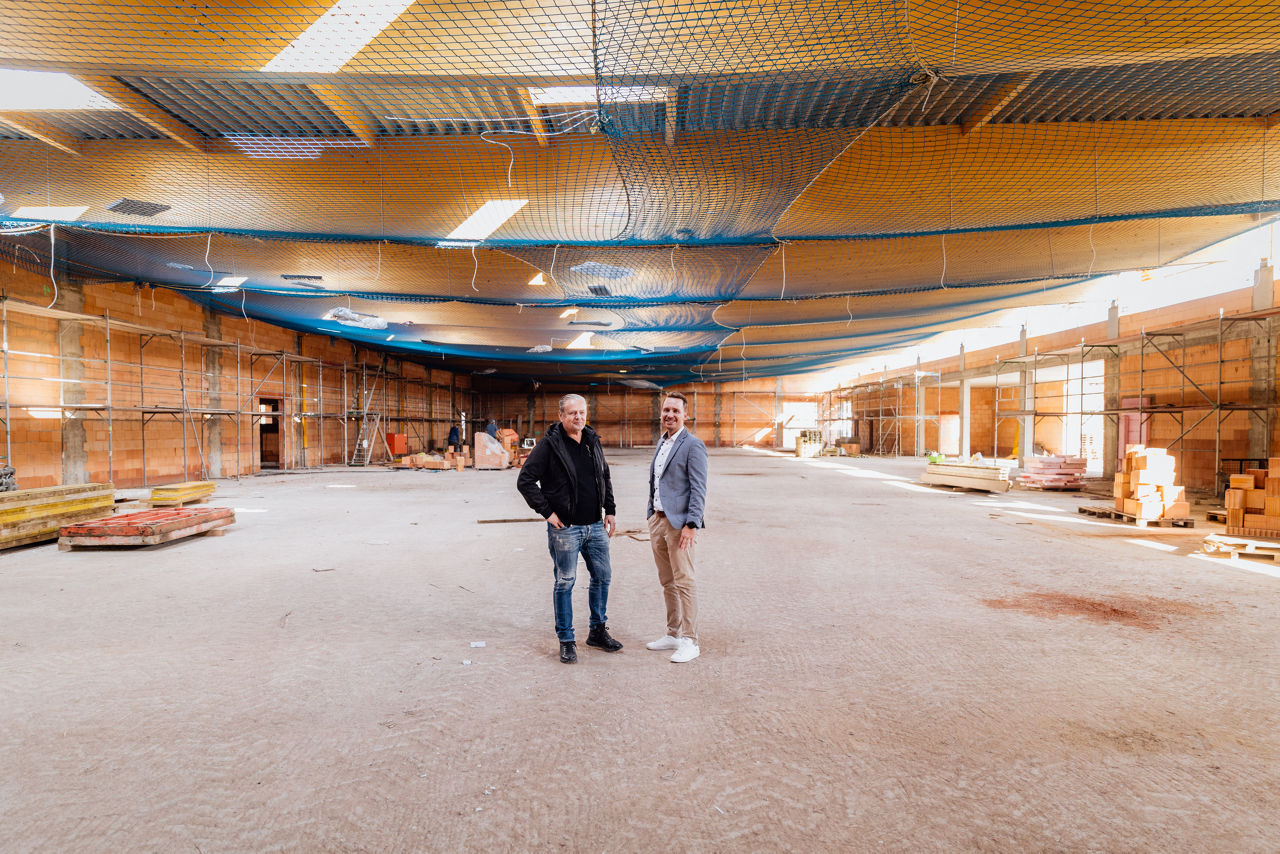 Innenaufnahme einer großen Hallenfläche eines Projekts von „PZ Marktbau“ während der Bauphase. Sichtbar sind die Deckenstruktur, aufgestellte Gerüste sowie gelagerte Baumaterialien im Innenbereich der Halle