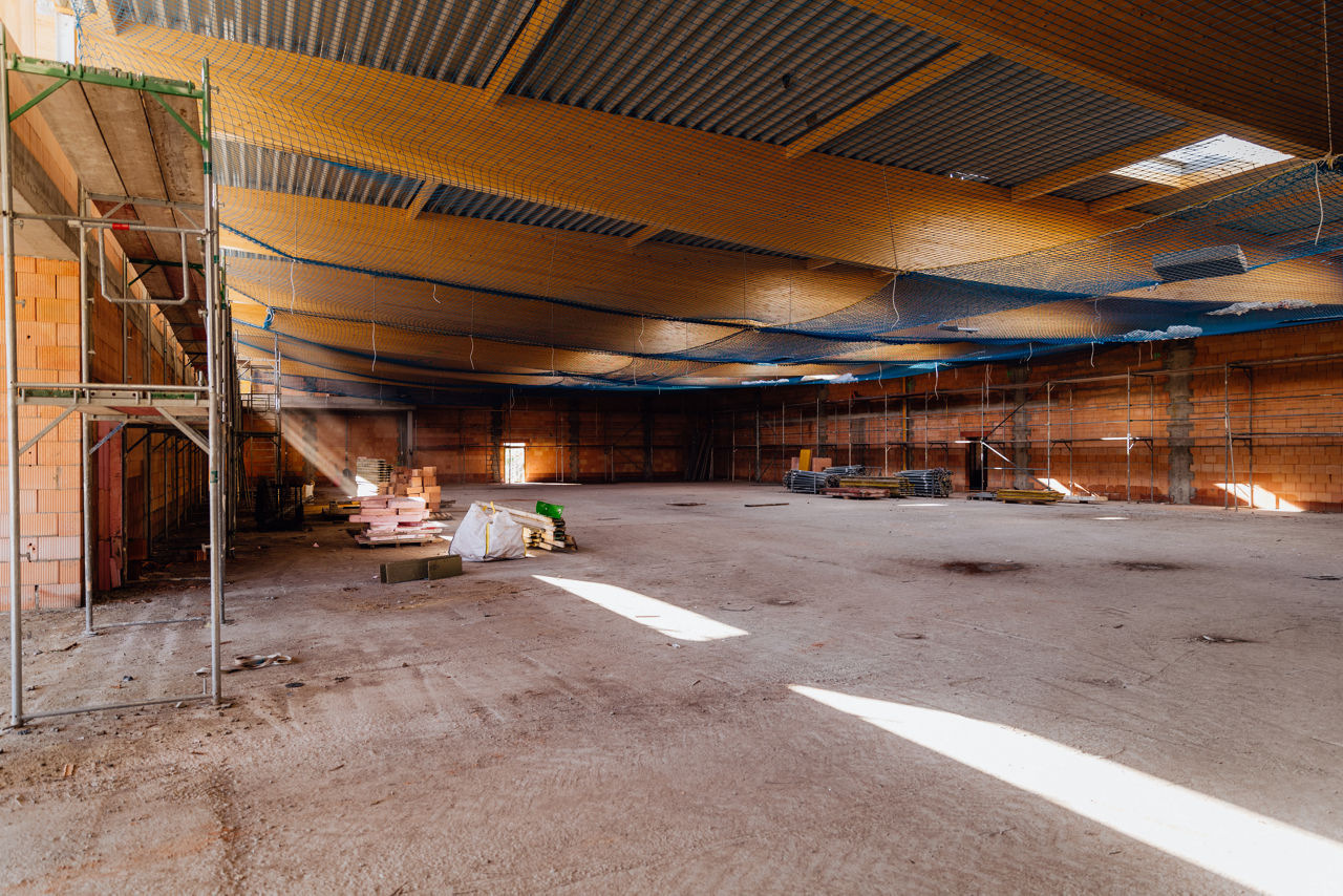 Innenaufnahme einer großen Hallenfläche eines Projekts von „PZ Marktbau“ während der Bauphase. Sichtbar sind die Deckenstruktur, aufgestellte Gerüste sowie gelagerte Baumaterialien im Innenbereich der Halle