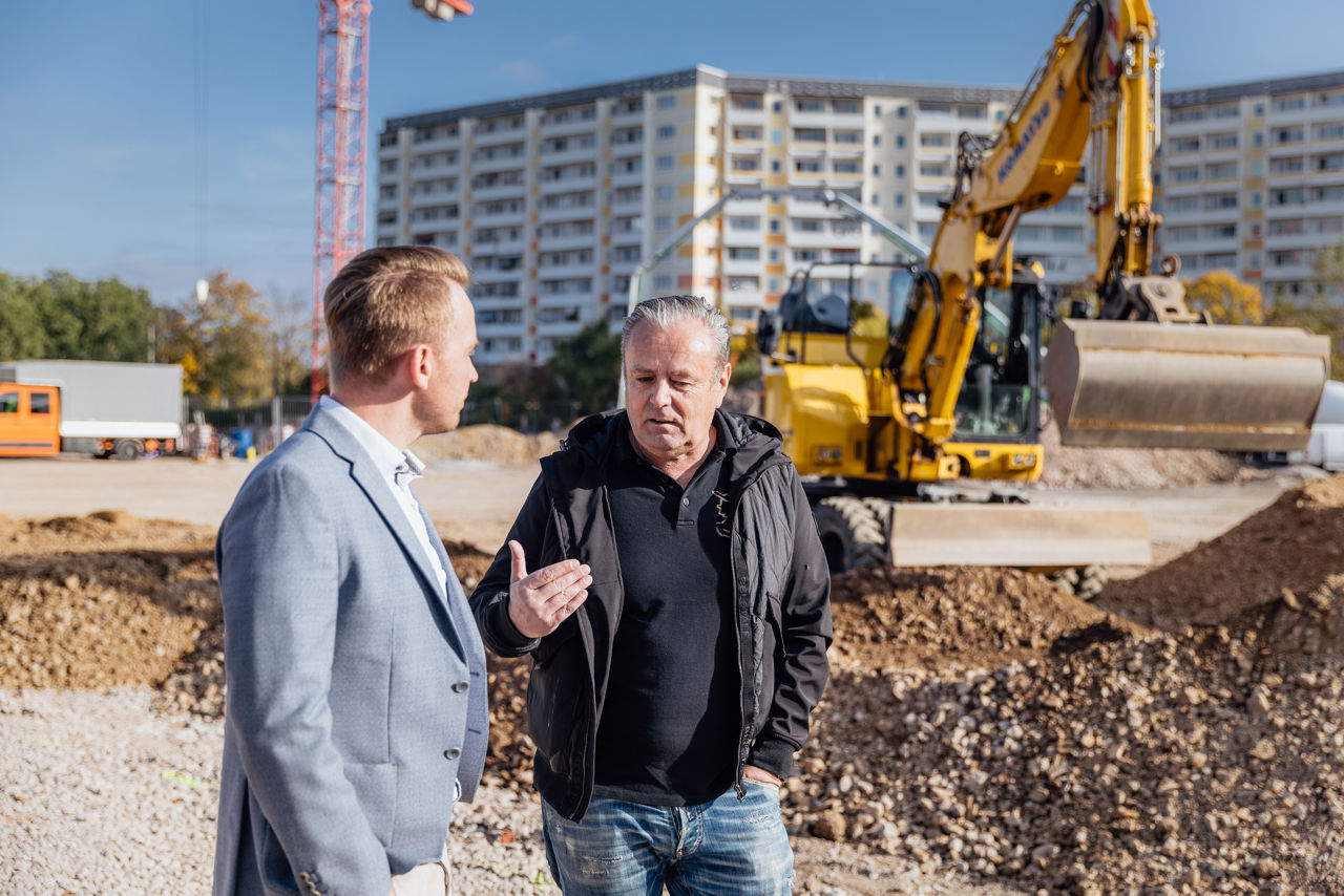 Baubesprechung auf der Baustelle eines Fachmarktprojekts von „PZ Marktbau“ mit Sicht auf laufende Erdarbeiten. Im Hintergrund sind ein Bagger sowie vorbereitete Flächen für den weiteren Baufortschritt des Fachmarktzentrums erkennbar