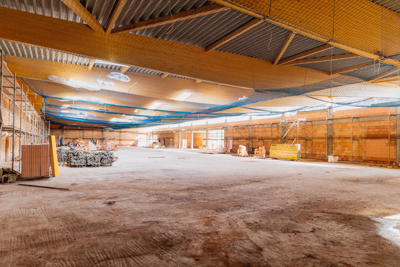 Innenansicht einer im Bau befindlichen Halle eines Fachmarktprojekts von „PZ Marktbau“ mit großflächigem Rohboden, sichtbaren Gerüststrukturen und Deckenabsicherung während der laufenden Bauphase des Fachmarktzentrums