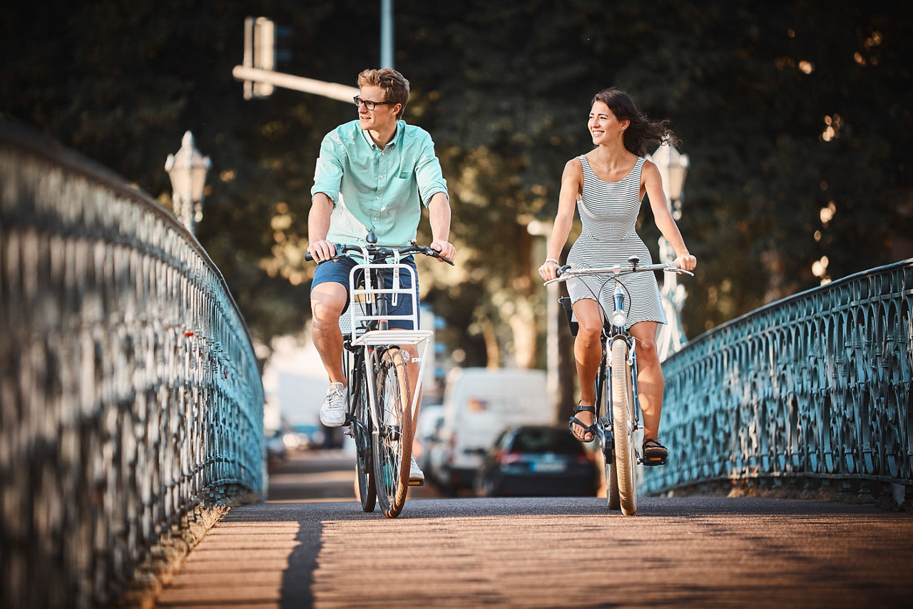 Eine Frau und ein Mann fahren nebeneinander auf Fahrrädern über eine verzierte Brücke in der Stadt.
