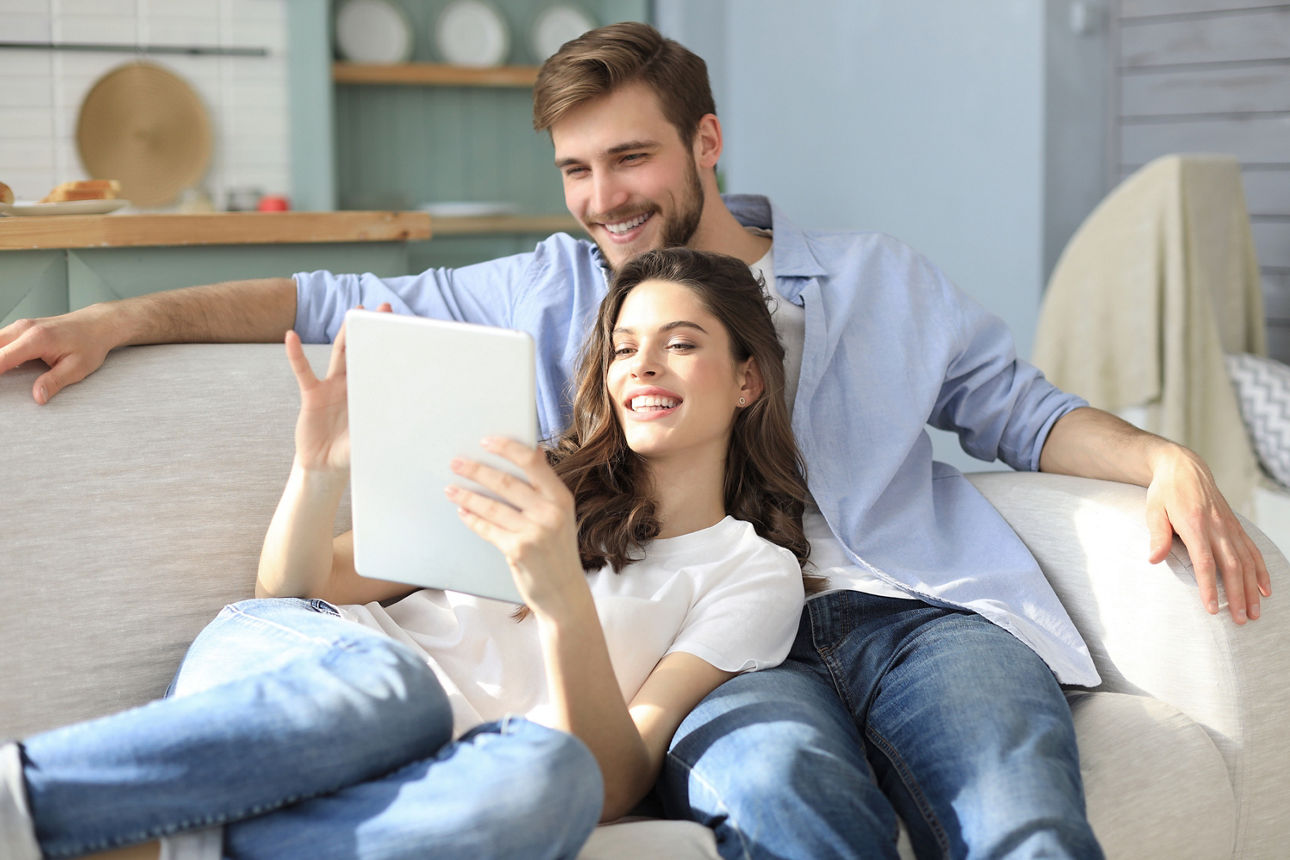 Jungens Paar sitzt bequem auf dem Sofa und schaut gemeinsam auf ein Tablet
