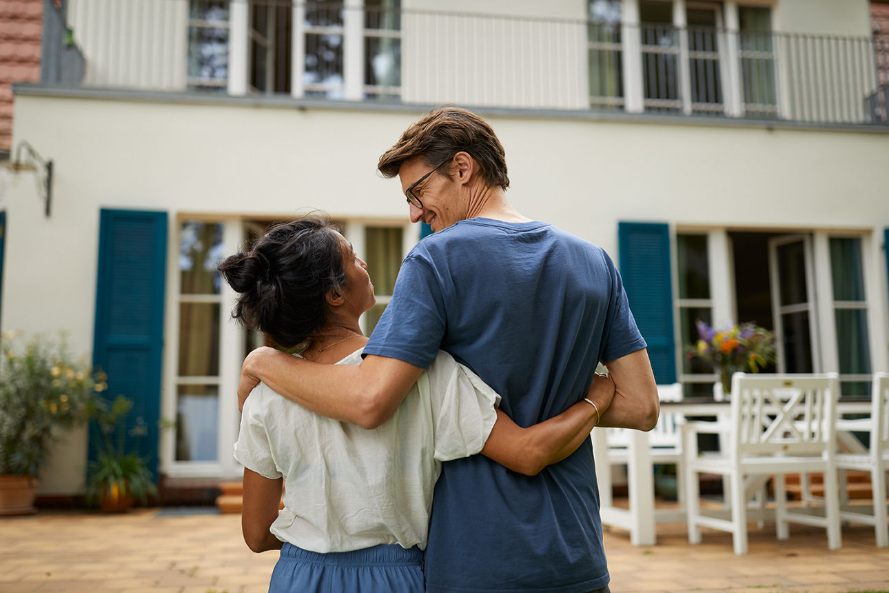 Ein Paar hält sich vorm neuen Haus im Arm