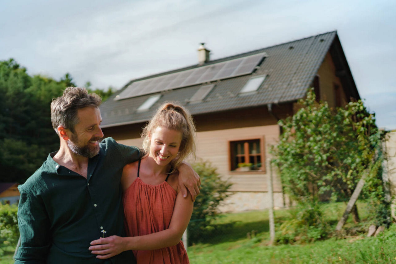 Glückliches Paar vor ihrem Haus mit PV-Anlage.