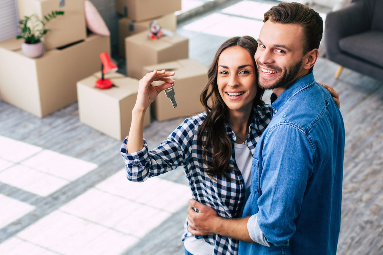 Junges Paar zeigt Schlüssel von neuem Eigenheim