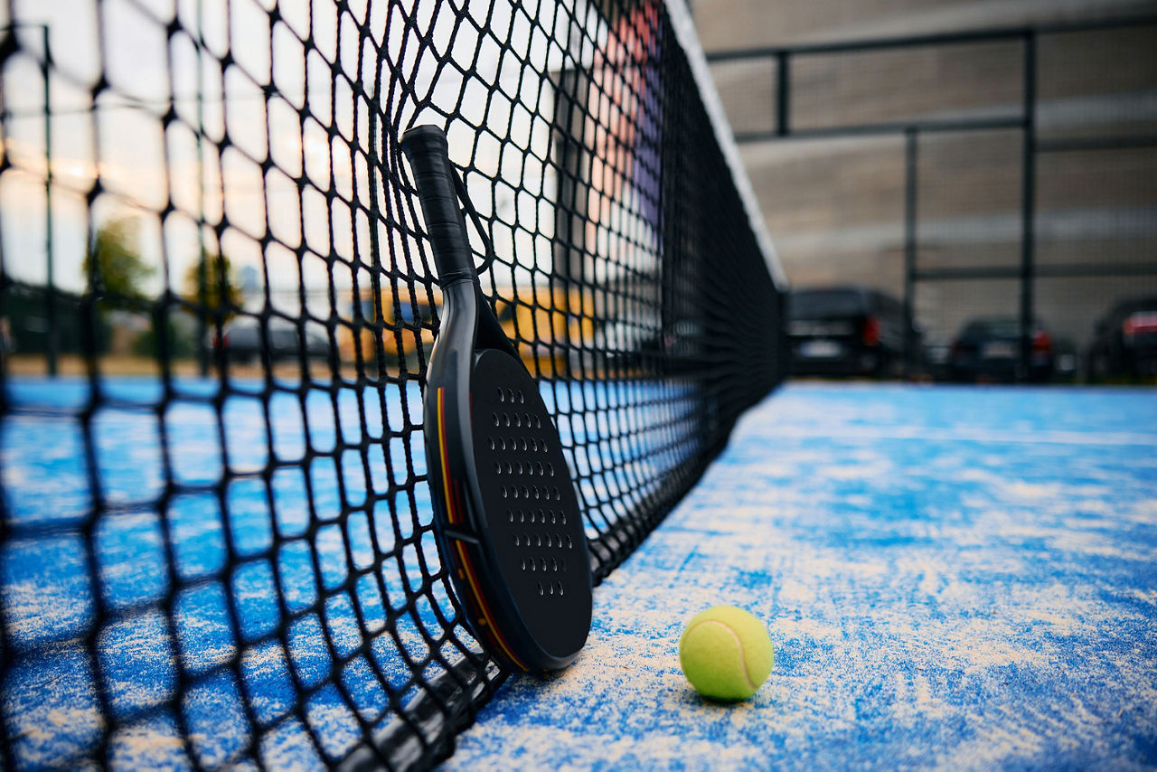 Padeltennisschläger und Ball auf einem Padelcourt.