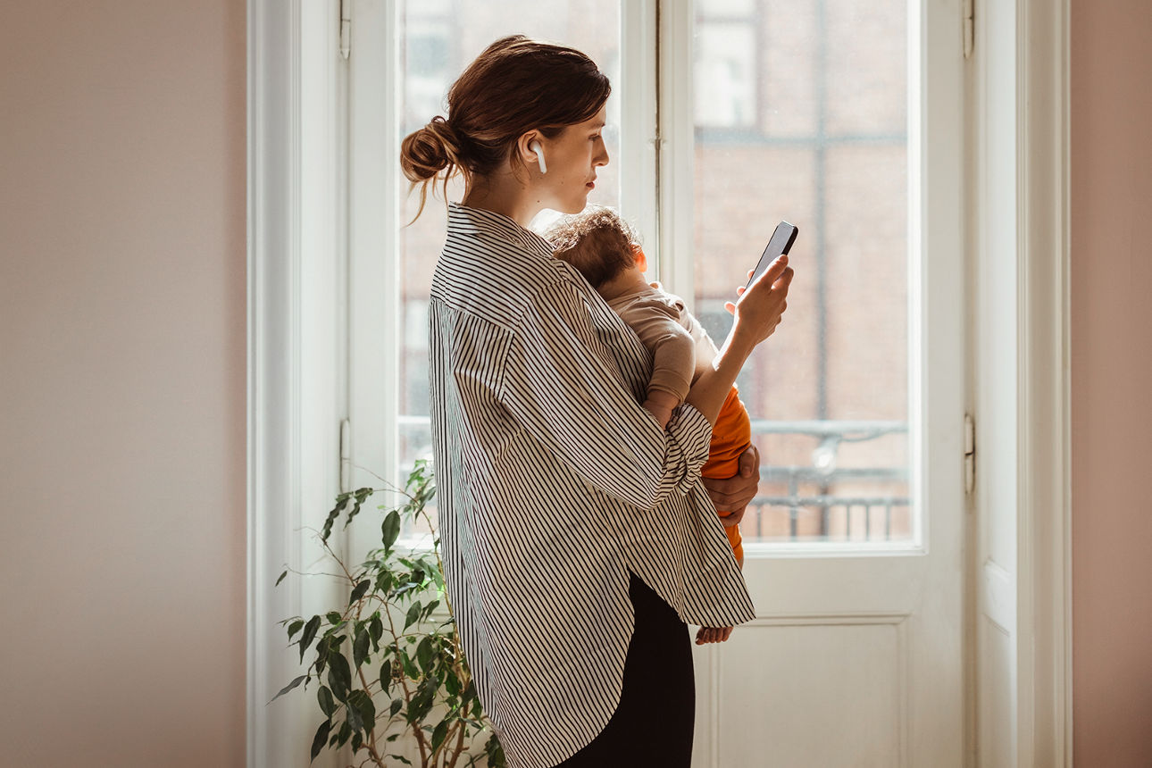 Frau mit Kind und Smartphone vor einem Fenster