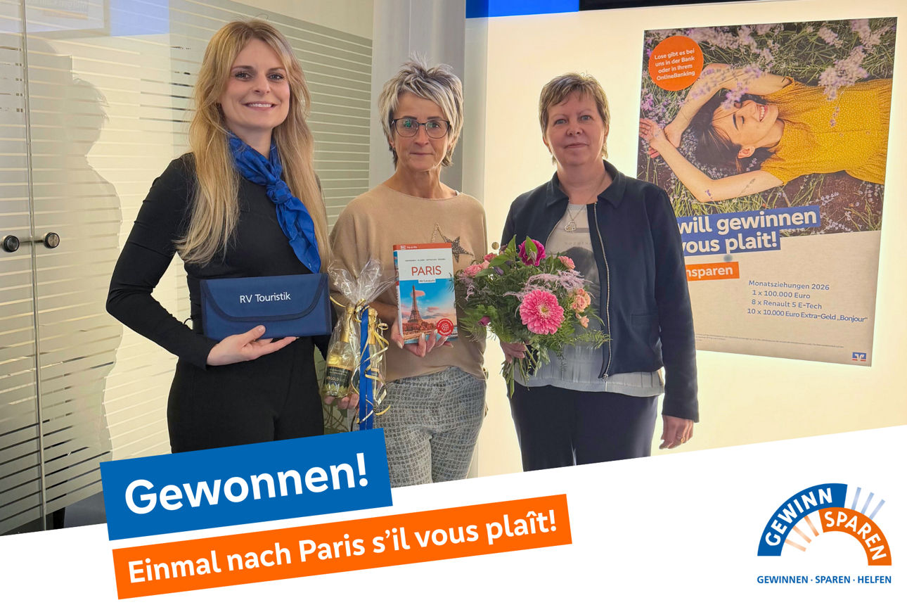 3 Frauen strahlen in die Kamera, sie stehen in einer Volksbank-Geschäftsstelle und halten Geschenke und Blumen
