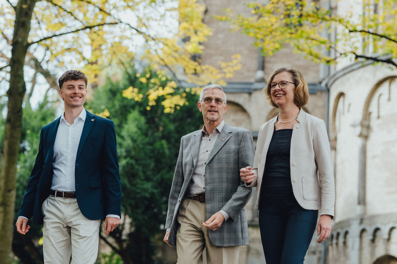 Drei Mitarbeitende laufen vor der St. Gereon Kirche in Köln entlang und unterhalten sich