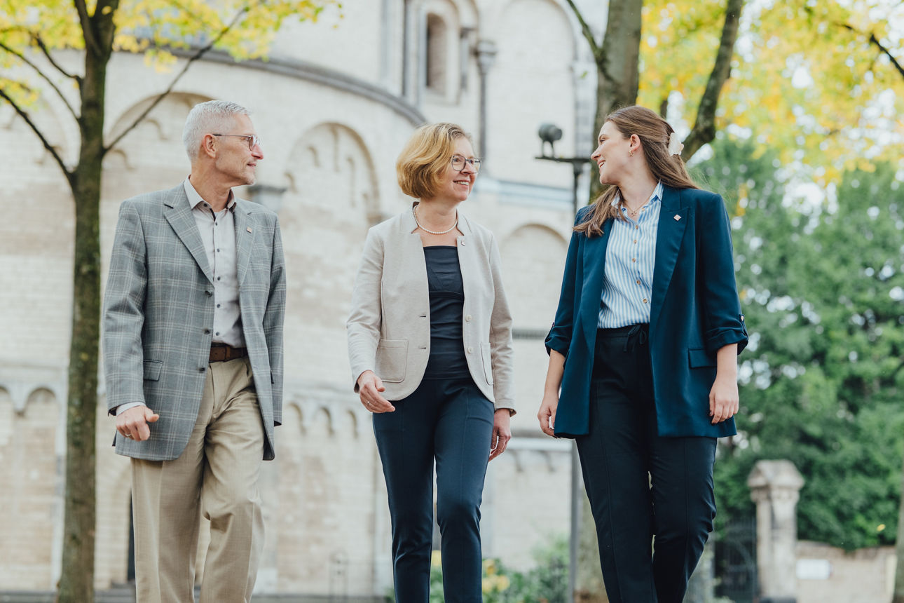 Drei Mitarbeitende stehen vor einer Kirche in Köln und unterhalten sich