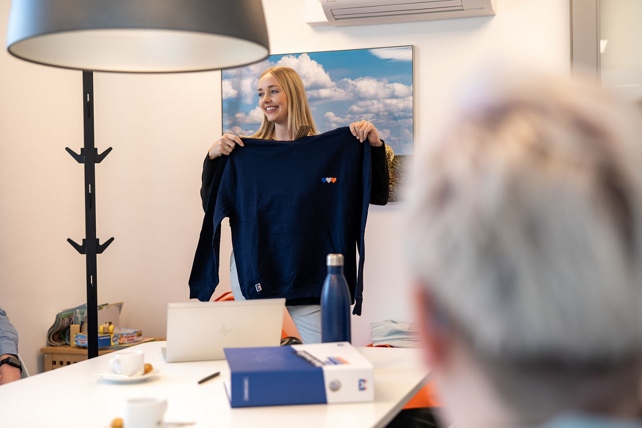 Mitarbeiterin zeigt einen Volksbank-Hoodie dem Team