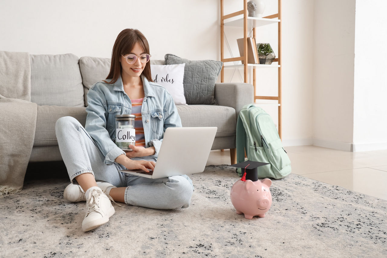 Junges Mädchen sitzen auf dem Boden mit Geld und Laptop