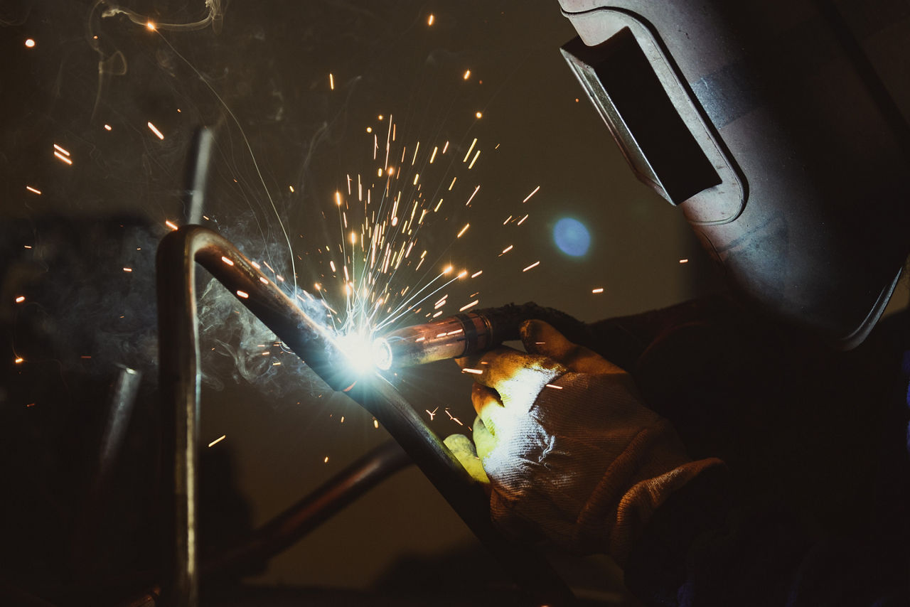 jemand mit Schweißtermaske lötet in einer Manufaktur Metall zusammen