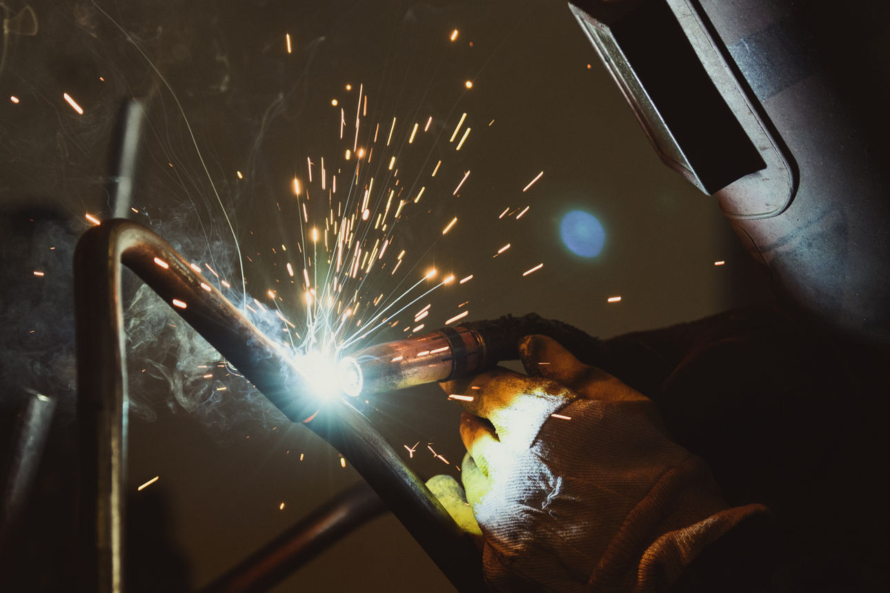 jemand mit Schweißtermaske lötet in einer Manufaktur Metall zusammen