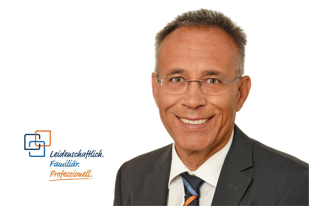 Porträt von Peter Rothdauscher, einem lächelnden Mann mit grauen Haaren, Brille im grauen Anzug mit orange-blau gestreifter Krawatte. Daneben das Firmenlogo und der Slogan "Leidenschaftlich. Familiär. Professionell."