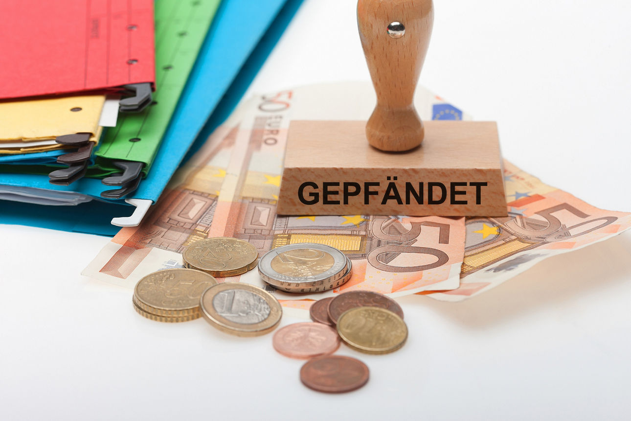 Geldscheine, Münzen, Aktenordner und ein gepfändet Stempel liegt auf dem Tisch